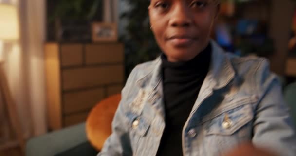De foto vangt een zelfverzekerde Afrikaanse vrouw met kort haar, comfortabel zittend in een goed verlichte woonkamer gericht op de taak bij de hand, met een camera schoonmaakdoek. - Video