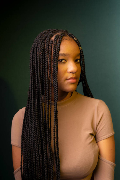 Young woman with braids, serious. Isolated on dark cyan background. - Fotó, kép