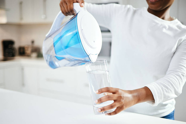 Person, jug and glass of filter water in kitchen for fresh drink, liquid and hydration. Closeup, thirsty woman or pouring pure aqua beverage in container for nutrition, drinking or filtration at home. - Foto, imagen