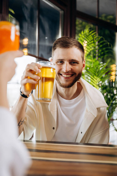 Sonriendo atractivo hombre está bebiendo cerveza mientras está sentado en el pub con amigos de la compañía - Foto, imagen