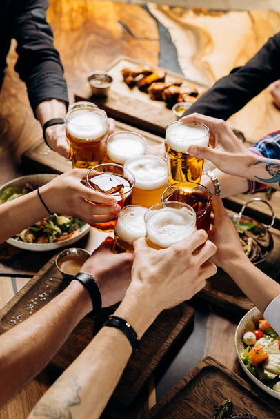 Freunde bejubeln Biergläser auf Holztisch mit leckerem Essen - Blick von oben auf Menschen, die in Bar-Restaurant feiern - Lifestylekonzept für Speisen und Getränke - Foto, Bild