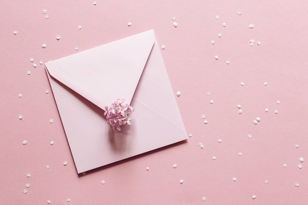 Blank greeting card mockup. Beige empty sheet of paper mockup in an pink envelope on pink paper background. flat lay. Wedding, business, birthday still life scene. Flower petals and lilac branch. - Φωτογραφία, εικόνα