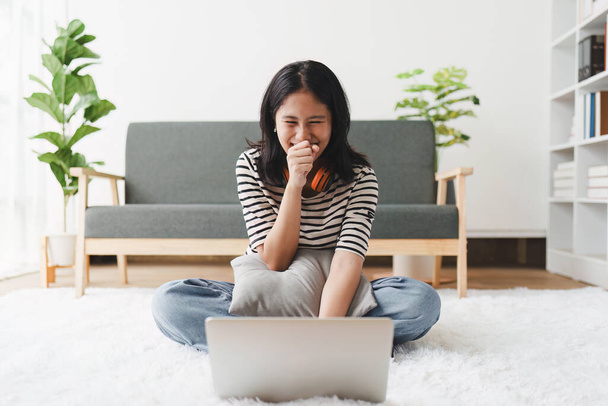 Junge asiatische entspannt lächelnde hübsche Frau entspannt mit Laptop zu Hause. Weibliche Glücksgefühle mit dem Handy auf der gemütlichen Couch. - Foto, Bild