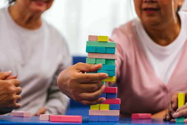Senior people playing a wooden block tower, risk and strategy of project management. Concept of business risk with domino blocks. Older People playing jenga block removal game on table at home - Photo, image