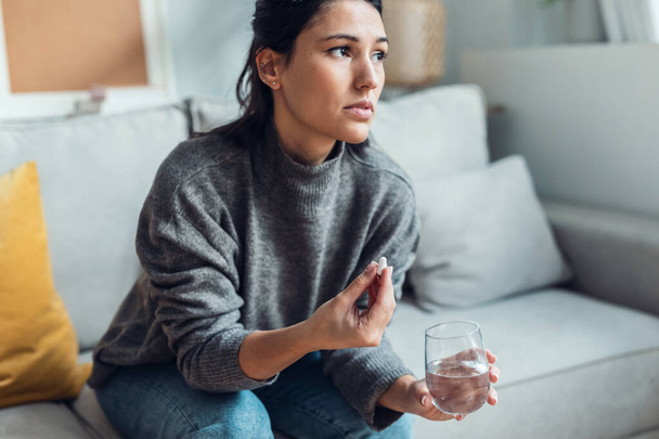 Shot of depressed sad woman taking pills while sitting on couch at home. - Foto, imagen