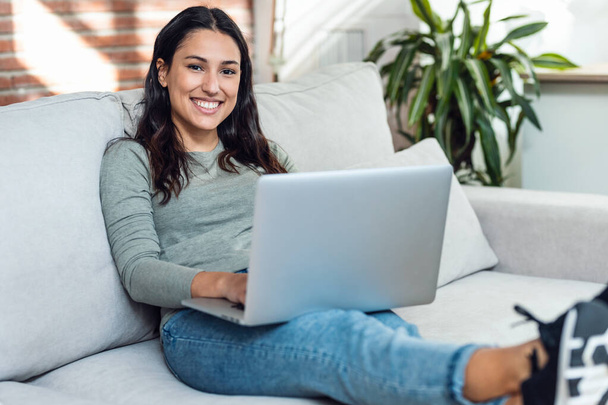Tiro de bela jovem mulher trabalhando com seu laptop enquanto sentado em um sofá em casa. - Foto, Imagem