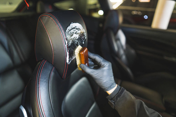 Closeup shot of interior car detailing of a leather car seat with a small brush and cleansing product. Blurred background. High quality photo - Foto, immagini