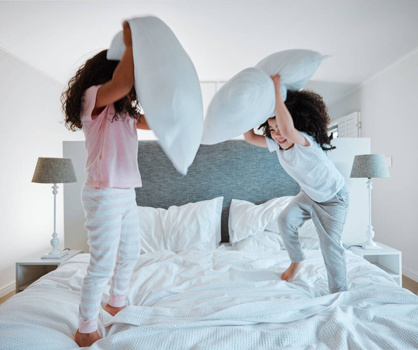 Boldog testvérek, párnacsaták és együtt játszanak az ágyon reggel, hogy jól érezzék magukat otthon. Kislányok, gyerekek vagy gyerekek élvezik játékos játék, szórakozás vagy harc párnák a hálószobában. - Fotó, kép