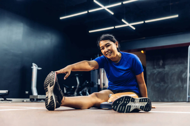 Athlete with prosthetic leg doing warm up exercise on GYM. Woman wearing prosthetic equipment for jogging at fitness Center. Female with prosthesis of leg. - Zdjęcie, obraz