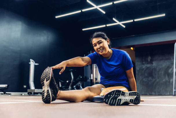 Athlete with prosthetic leg doing warm up exercise on GYM. Woman wearing prosthetic equipment for jogging at fitness Center. Female with prosthesis of leg. - Foto, afbeelding