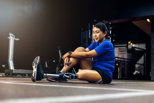 Athlete with prosthetic leg doing warm up exercise on GYM. Woman wearing prosthetic equipment for jogging at fitness Center. Female with prosthesis of leg. - Фото, изображение