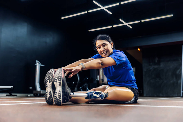 Athlete with prosthetic leg doing warm up exercise on GYM. Woman wearing prosthetic equipment for jogging at fitness Center. Female with prosthesis of leg. - Valokuva, kuva