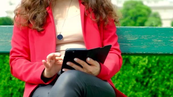 Eine Frau benutzt ihr Handy, während sie auf einer Bank im Park sitzt - Filmmaterial, Video