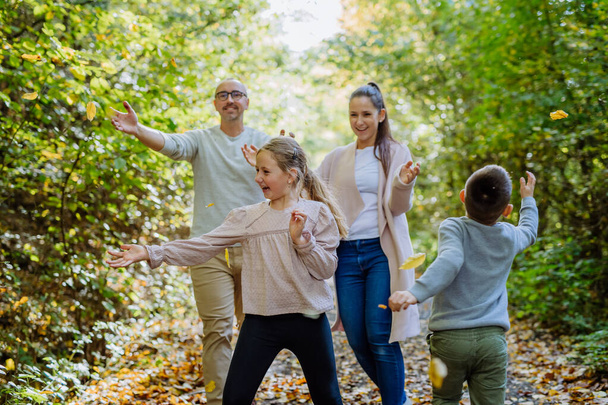 Щаслива сім'я розважається з листям в осінньому лісі. - Фото, зображення