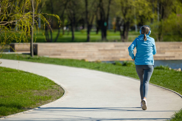 Jogging. Woman in blue blazer listening to the music and jogging - Фото, зображення