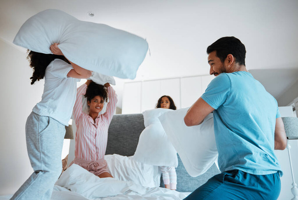 Happy family, pillow fight and morning play on bed together for fun bonding weekend at home. Father, mother and playful children enjoying game, entertainment or fighting with pillows in the bedroom. - Foto, afbeelding