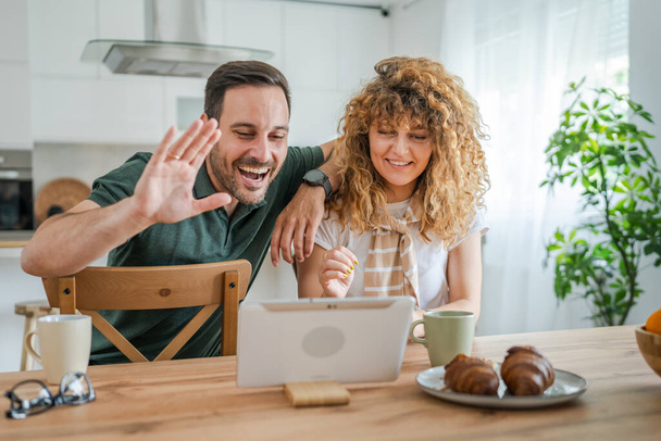 Καυκάσιος ζευγάρι άντρας και γυναίκα σύζυγος και γυναίκα χρησιμοποιούν ψηφιακή ταμπλέτα για να κάνουν μια βιντεοκλήση μιλώντας στο διαδίκτυο, ενώ διασκεδάζουν στο σπίτι οικογενειακή ζωή έννοια αντίγραφο χώρο πραγματικό άνθρωποι - Φωτογραφία, εικόνα