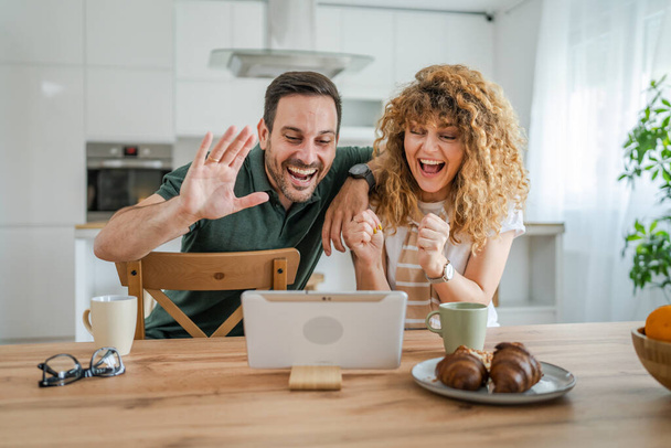 Καυκάσιος ζευγάρι άντρας και γυναίκα σύζυγος και γυναίκα χρησιμοποιούν ψηφιακή ταμπλέτα για να κάνουν μια βιντεοκλήση μιλώντας στο διαδίκτυο, ενώ διασκεδάζουν στο σπίτι οικογενειακή ζωή έννοια αντίγραφο χώρο πραγματικό άνθρωποι - Φωτογραφία, εικόνα