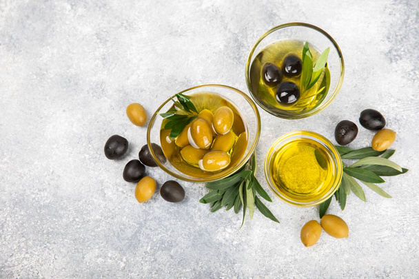 Olivenöl in einer Glasschüssel und Sauce Boot auf einem strukturierten Hintergrund. Ölflasche mit Zweigen und Früchten von Oliven. Platz für Text. Kopierraum. Speiseöl und Salatdressing. - Foto, Bild