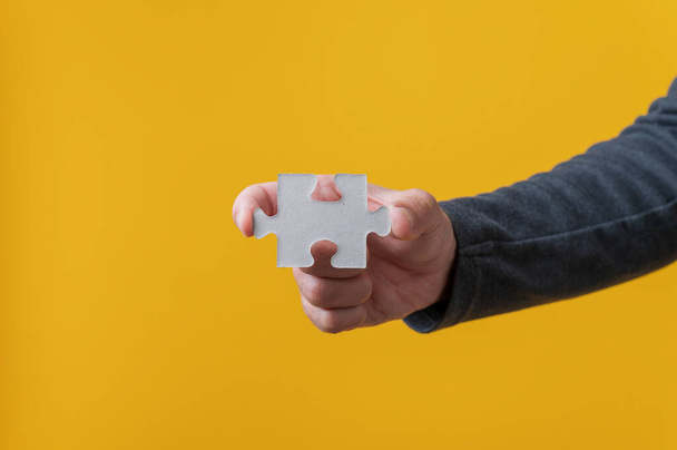 Mužská ruka drží prázdný puzzle kus přes jasně žluté pozadí. - Fotografie, Obrázek