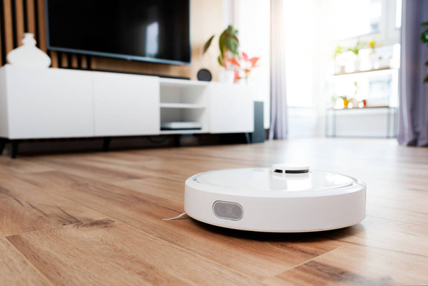 White robot vaccum cleaner on the floor in the living room, smart home device - Photo, image