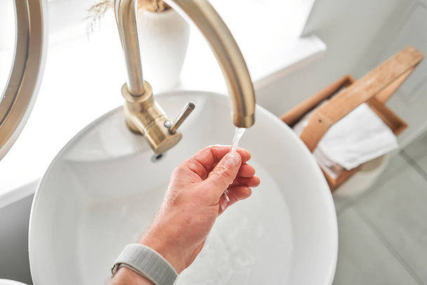Kézi mosás csapvízzel a mosdó felett a modern fürdőszobában. Forgó fúvóka a keverőn a víz áramlásának beállításához. Fehér mosdókagyló kézmosáshoz. kiváló minőségű fénykép - Fotó, kép
