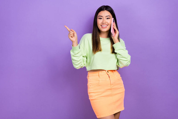 Photo of pretty shiny lady wear green sweatshirt speaking modern gadget showing empty space isolated purple color background. - Foto, Imagem