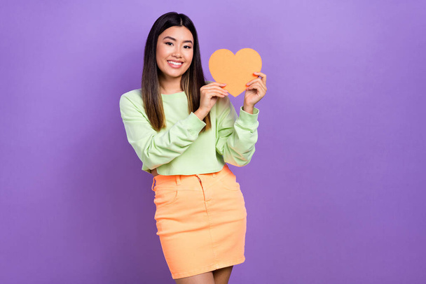 Photo of candid sincere nice woman with dyed hairdo dressed green shirt fingers hold paper heart isolated on purple color background. - Foto, Imagen