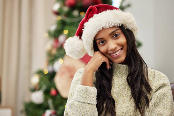 Mujer feliz, retrato y sombrero de Navidad para la temporada festiva, celebración o regalo dando tiempo en casa. El rostro de la persona femenina con la sonrisa en el descanso para las vacaciones, el fin de semana o la fiesta de diciembre por el árbol en casa. - Foto, imagen
