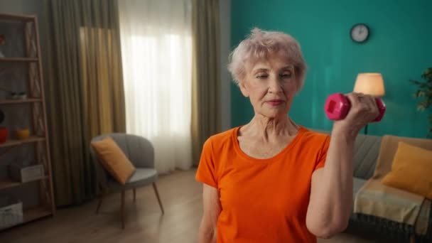 Portrait of a grayhaired elderly woman doing fitness exercises with dumbbells at home close up. A mature woman pumps up her biceps, trains her triceps, keeps her arm muscles in good shape. Sports for - Séquence, vidéo