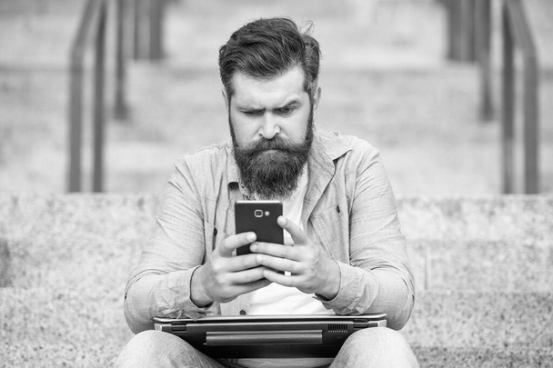 Serious man chatting on mobile phone while sitting on steps outdoors. Chatting online on mobile device. Chatting using mobile apps in smartphone. Mobile communication. - Fotoğraf, Görsel