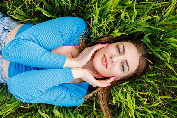 Happy young woman lies on green grass and enjoys nature. Smiling attractive woman in green grass - Foto, Bild