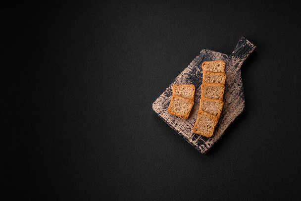 Deliciosos croutons de trigo retangular salgado com sal e especiarias em um fundo de concreto escuro - Foto, Imagem