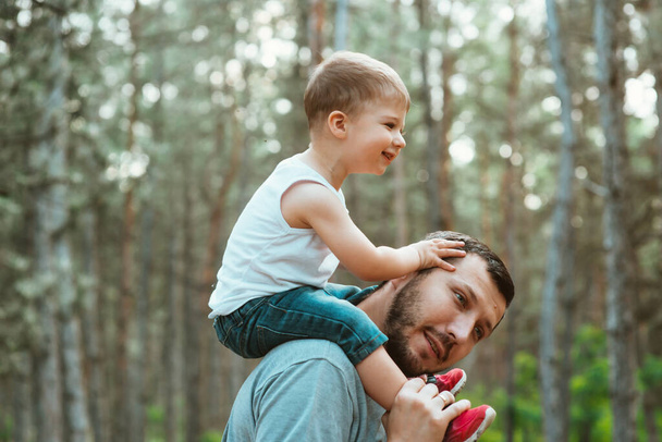 father's day. Happy European-looking father walks with his young cute two-year-old son on his shoulders in the woods. Fatherhood, a happy childhood. Happy summer time. Family concept - Fotoğraf, Görsel