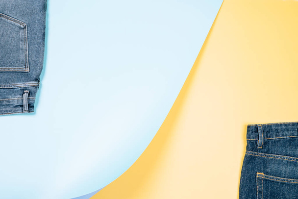 Composición de moda con parte de los vaqueros nuevos sobre fondo azul claro y amarillo pastel. Fondo denim abstracto. Tienda de mezclilla, tienda, venta, reciclaje de fondo. - Foto, Imagen