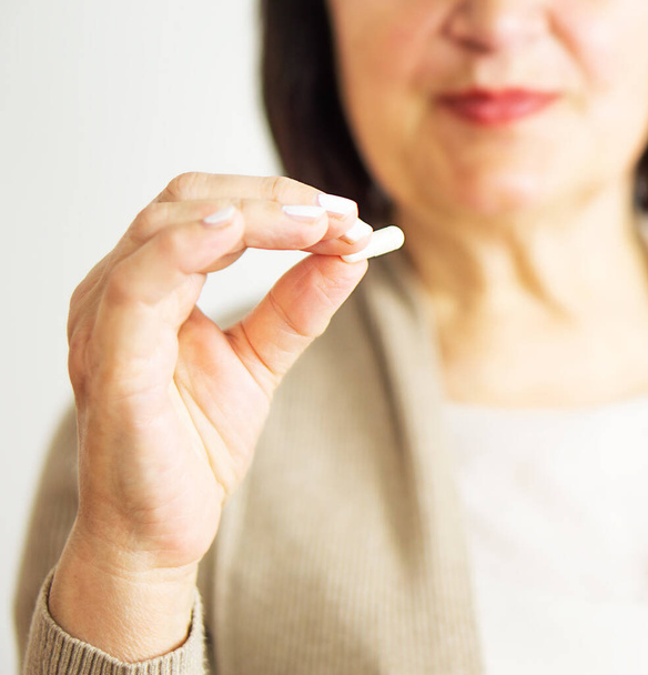 A portrait of a retired woman in casual clothes at home holding her medication. Healthy middle aged 60s woman holding a tablet. Happy adult woman taking vitamin pill. - Photo, Image