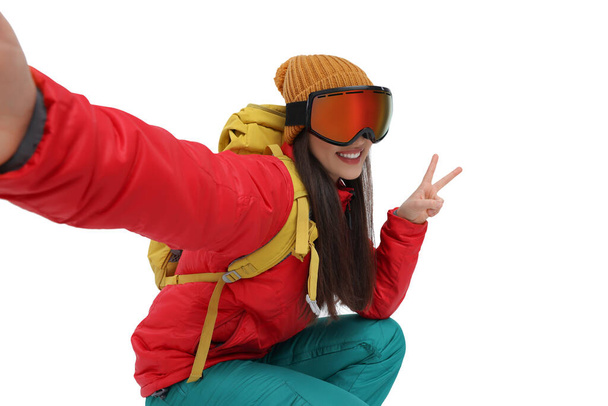 Smiling woman in ski goggles taking selfie and showing peace sign on white background - Foto, Bild