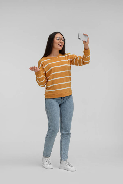 Smiling young woman taking selfie with smartphone on white background - Fotografie, Obrázek
