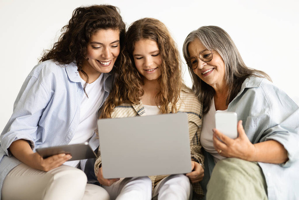 Glimlachende Europese oude, volwassen en tiener vrouw met smartphone, tablet en laptop hebben videogesprek, geïsoleerd op witte muur achtergrond, studio. Apparaat, sociale netwerken van apps, familierelaties - Foto, afbeelding