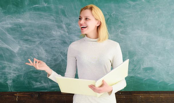 Χαμογελώντας γυναίκα δάσκαλος με σημειωματάριο στέκεται κοντά μαυροπίνακα δίνοντας μάθημα. Ευτυχισμένος μαθητής ή δάσκαλος στην τάξη. Εκπαίδευση σε πανεπιστήμιο λυκείου. Πίσω στο σχολείο. Παγκόσμια ημέρα δασκάλων - Φωτογραφία, εικόνα