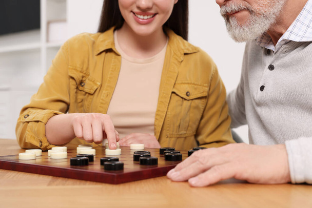 Playing checkers. Senior man learning woman at table in room, closeup - Foto, Bild