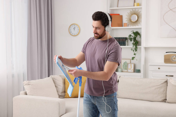 Spring cleaning. Man with headphones and mop in living room - Fotografie, Obrázek