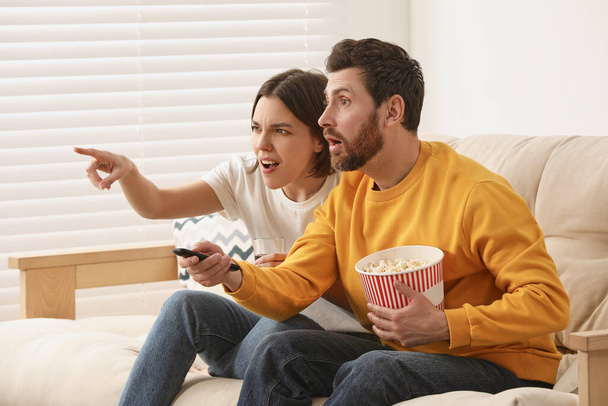 Emotional couple watching TV with popcorn on sofa - Foto, afbeelding