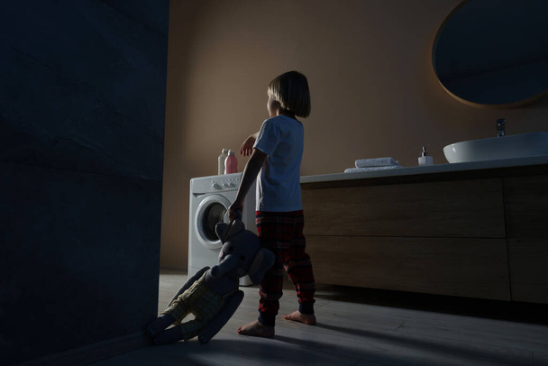 Boy in pajamas with toy elephant sleepwalking indoors at night - Foto, afbeelding
