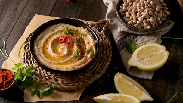 Delicious hummus in ceramic bowl. Colorful snack composition on a black wooden background. - Φωτογραφία, εικόνα