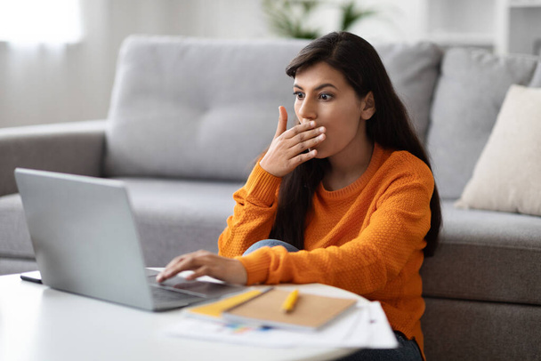 Bug, error, broken app. Shocked emotional pretty young indian woman looking at laptop screen and cover her mouth, freelancer have difficulties with software, home interior - Fotoğraf, Görsel