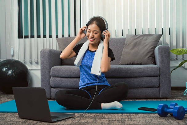 Asian beautiful young woman using laptop and headphones listen music while practicing exercise yoga at home. - Valokuva, kuva