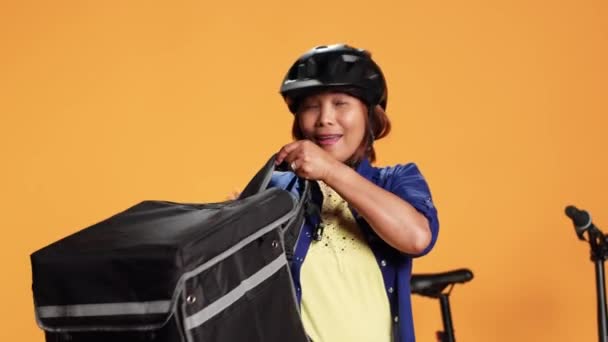 Close up shot of courier arriving to customer address, taking meal bag out of thermic backpack. Happy BIPOC bike rider delivering lunch to client, isolated over studio background - Footage, Video