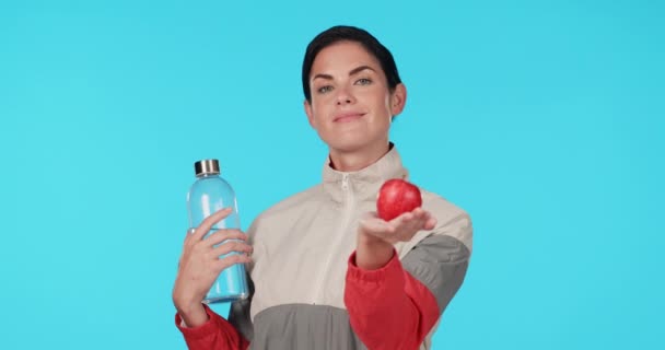 Υγεία, πρόσωπο και γυναίκα με ένα μήλο σε μπλε φόντο με νερό για διατροφή και διατροφή. Χαμόγελο, ευεξία και πορτρέτο του κοριτσιού με φρούτα και μπουκάλι για fitness detox απομονωμένο σε φόντο στούντιο. - Πλάνα, βίντεο