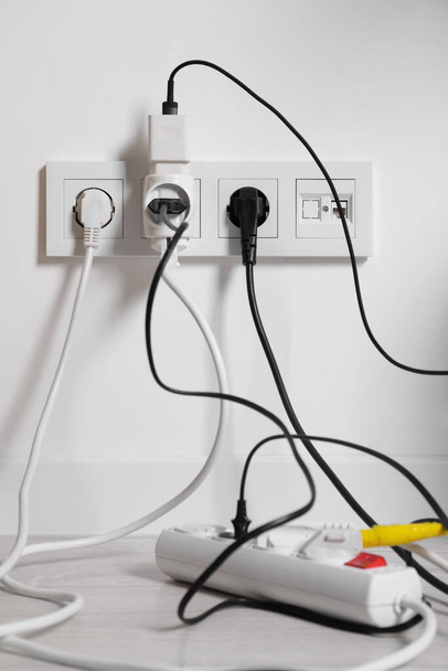 Different electrical plugs in socket and power strip on floor indoors - Fotó, kép